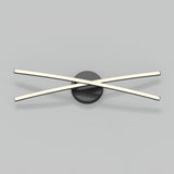 Minimalist wall light fixture with two slim, illuminated bars crossing over each other in an X shape, mounted on a round, black base against a plain gray background.