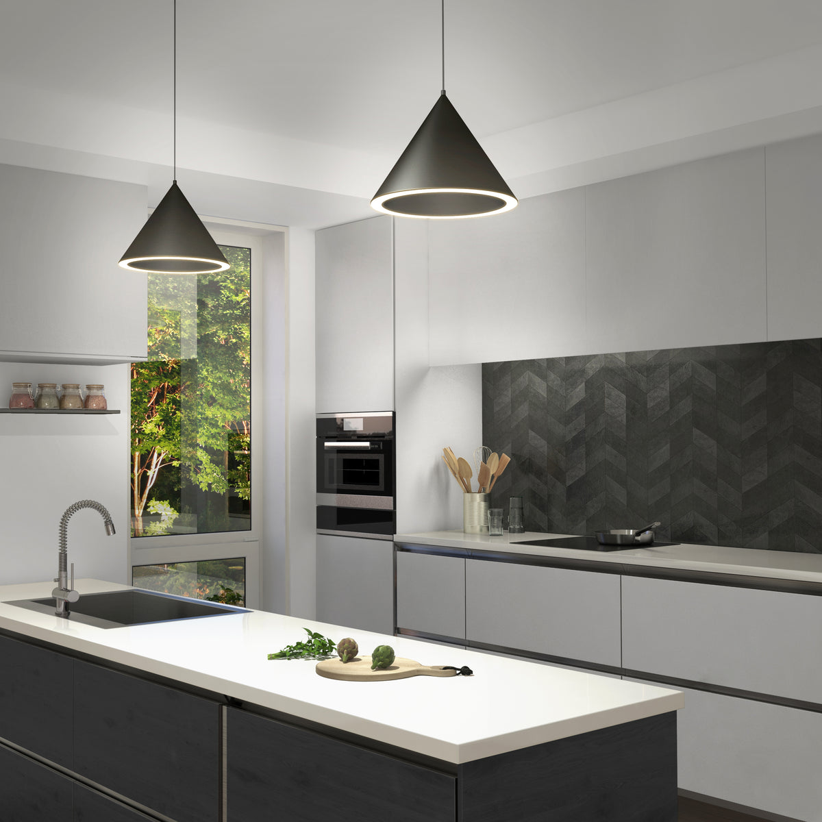 Modern kitchen with white cabinets, a dark herringbone backsplash, and a large island with a sink. Two pendant lights hang above the island. A window reveals greenery outside. Cooking utensils sit on the counter.