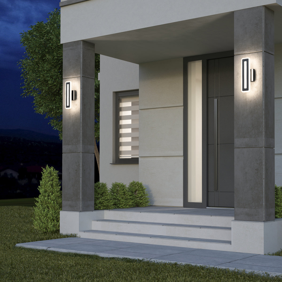 Modern house entrance at dusk with illuminated wall lights on either side of the door, concrete columns, steps leading to the door, a large window with a striped blind, and neatly trimmed bushes and grass.