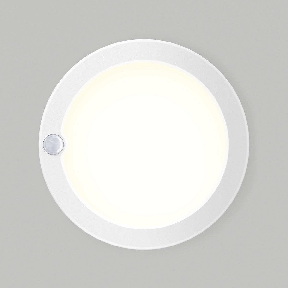 A round, white ceiling light with a small sensor on its edge is mounted on a plain gray wall and emits a bright, even glow.