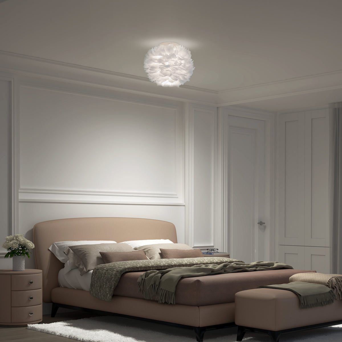 A neatly arranged modern bedroom with a beige upholstered bed, green bedding, matching ottoman, nightstand with flowers, and a white feathered ceiling light illuminating the space.