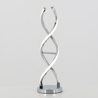 The Artika Swirl LED table lamp features a twisted double-helix metal design and integrated LED light, resting on a round chrome-finished base, displayed against a plain light background.