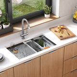 A modern kitchen sink with a drying rack, glass, and fresh produce beside a cutting board with sliced fruit. There are potted plants and lemons on the counter near a large window.