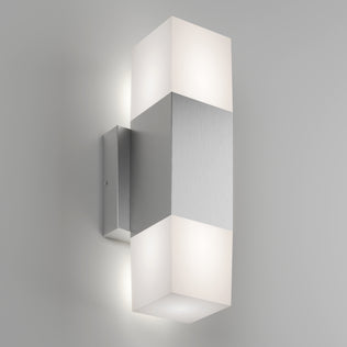 The Artika Lennox indoor-outdoor LED wall light 3 CCT features a brushed metal center and frosted rectangular diffusers that emit soft upward and downward light, shown mounted on a light gray wall.