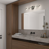 Modern bathroom with wood cabinets, a large mirror, a wave-shaped wall light above it, a gray countertop with a built-in sink, a folded towel, and a vase with dried flowers.