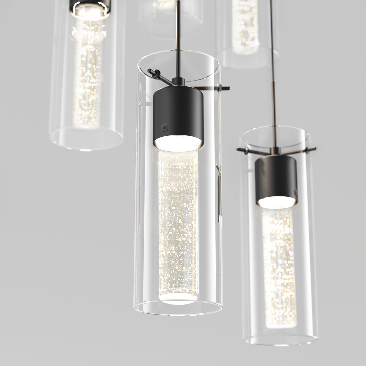 Close-up of modern pendant lights with cylindrical glass shades and inner lights featuring a textured, sparkling pattern, suspended from the ceiling against a light gray background.