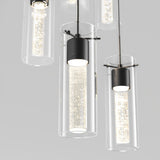 Close-up of modern pendant lights with cylindrical glass shades and inner lights featuring a textured, sparkling pattern, suspended from the ceiling against a light gray background.