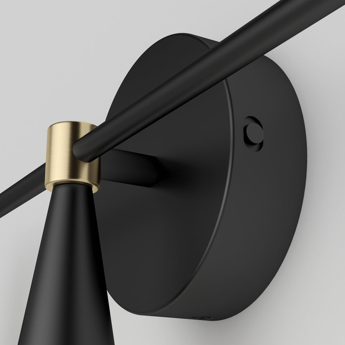 Close-up of a modern black wall-mounted light fixture with a round base and a gold accent where the rod meets the base, set against a plain light background.