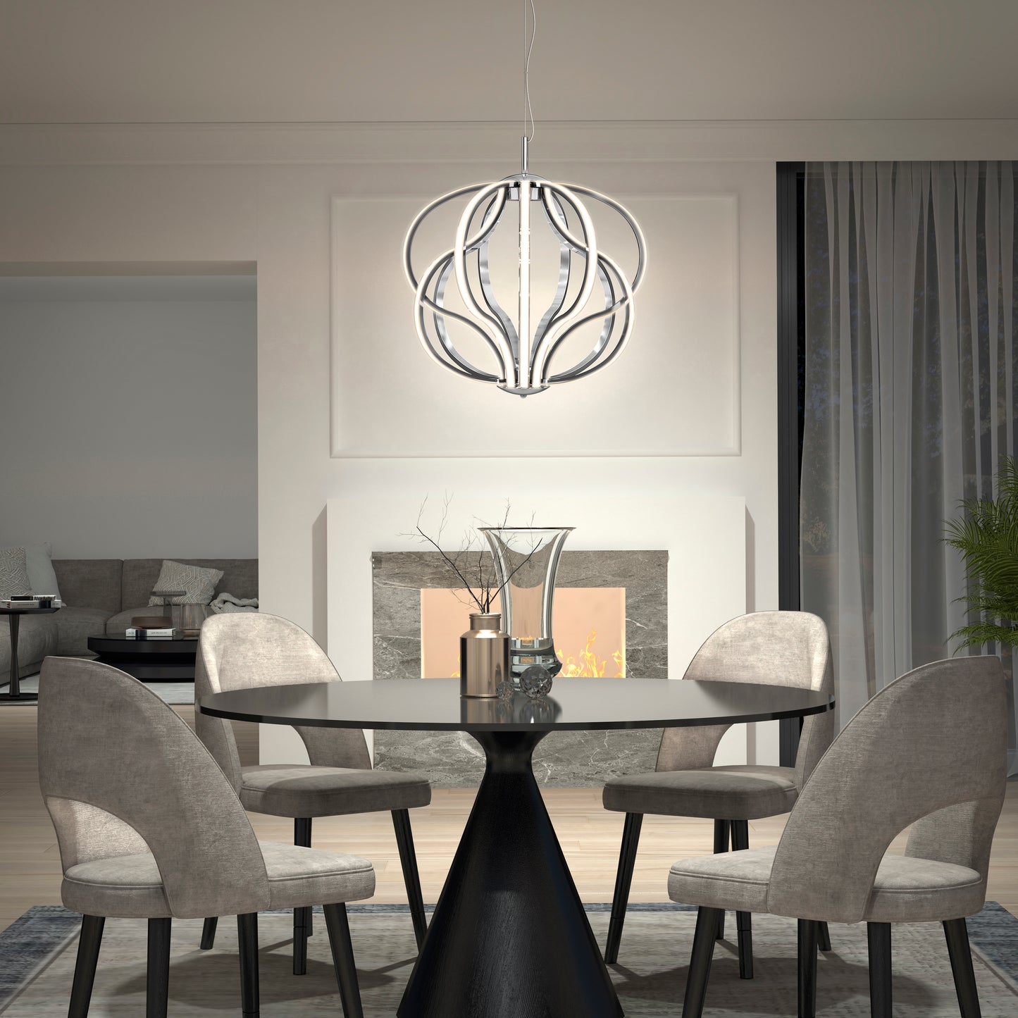 A modern dining room features a round black table, four gray upholstered chairs, a decorative centerpiece, and the Artika Meridian LED pendant light. In the background, a lit fireplace and cozy living area can be seen.