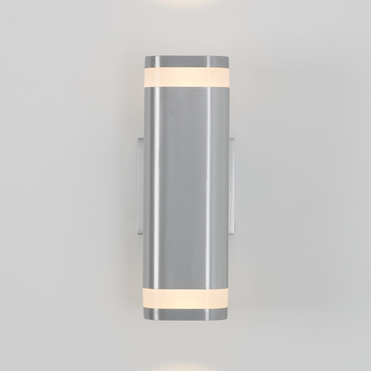 A modern wall sconce with a cylindrical brushed metal body and frosted glass bands at the top and bottom, emitting soft light upward and downward, mounted on a light gray wall.