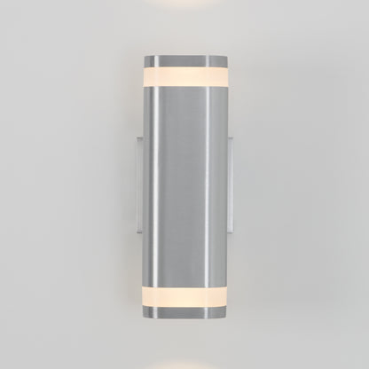 The Artika Mettle LED indoor-outdoor wall light features a modern cylindrical brushed metal body with frosted bands at the top and bottom, emitting soft light from both ends and shown mounted on a light gray wall.