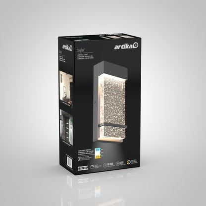 A black and gray Artika retail box for the Skyler indoor-outdoor LED wall light, showing the modern rectangular fixture with textured illuminated panel, plus product details and specs on the packaging.
