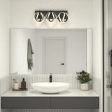 Modern bathroom with a round white sink, black faucet, potted plant, soap dispensers, a towel on the wall, and a large mirror reflecting a white door. Above the mirror is a contemporary three-light fixture.