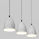 Three modern pendant lights with smooth, speckled gray concrete shades hang from black cords against a plain light gray background. The lights are lit, casting a soft white glow downward.