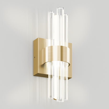 The Dorado LED Contemporary Wall Sconce by Artika features a brushed gold rectangular base and clear vertical glass rods, emitting soft white light, and is shown mounted on a plain light-colored wall.