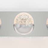 A modern light fixture with a half-globe design; the top half is a clear dome with bubble-like patterns inside, and the bottom half is smooth, reflective metal. The fixture is mounted on a sleek, metallic surface.