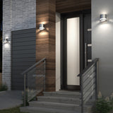 Modern front door entryway with wooden and gray brick walls, illuminated by three sleek wall-mounted lights, and metal railings on stairs leading up to the entrance.