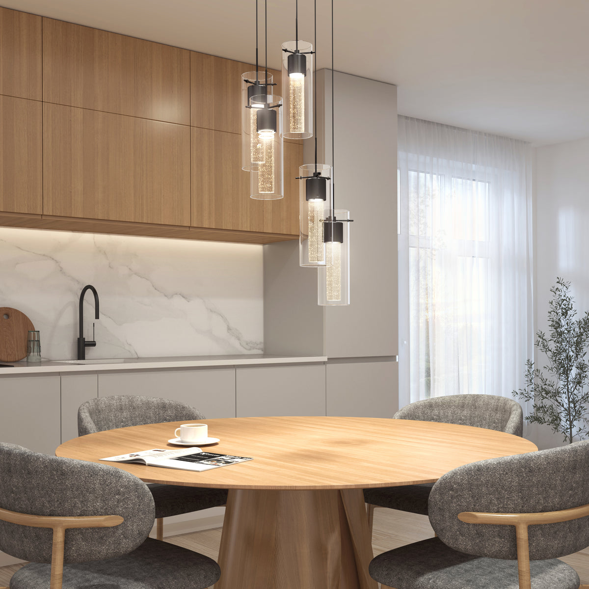 Modern kitchen with light wood cabinets, marble backsplash, and round wooden dining table set with four gray chairs. Pendant lights hang above the table; a cup and saucer rest on the table. Soft natural light fills the room.