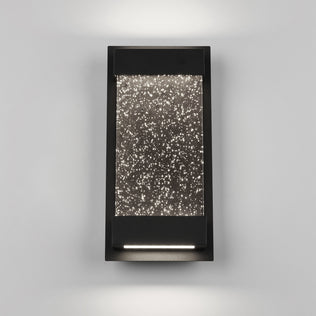 The Artika Essence Glow Box indoor-outdoor LED wall light features a modern rectangular design with a black frame and star-textured illuminated glass, casting soft up-and-down lighting against a light gray wall.