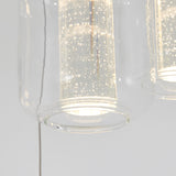 A close-up of a modern pendant light with a clear glass shade, revealing a glowing cylindrical inner light fixture with small bubble-like details inside.