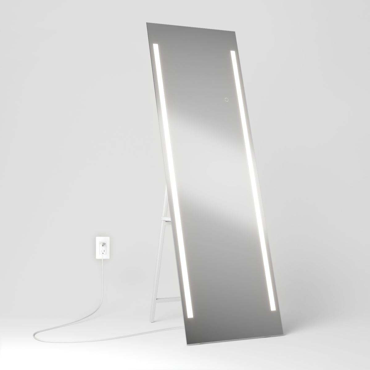 A tall rectangular mirror with two vertical LED light strips stands on the floor, propped up on a white support. A white power cord is plugged into a nearby wall outlet against a plain white background.