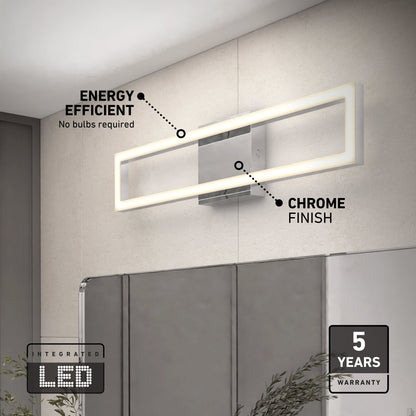 The Artika-CAN-dev Dover modern LED bathroom vanity light 5 CCT, featuring a chrome finish, is mounted above a bathroom mirror. Labels note its energy efficiency, integrated LED, and 5-year warranty. A plant sits in the lower right corner.