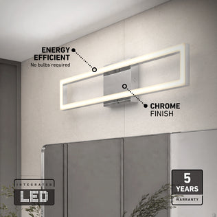 The Artika Dover modern LED bathroom vanity light 5 CCT, with a sleek chrome finish and integrated LED, is mounted above a mirror. Text notes its energy efficiency and 5-year warranty. Green plants appear at the bottom of the image.
