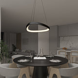 A modern dining room with a round black table set for four, wooden chairs, a sleek oval pendant light above, and an open kitchen with bar stools and marble backsplash in the background.