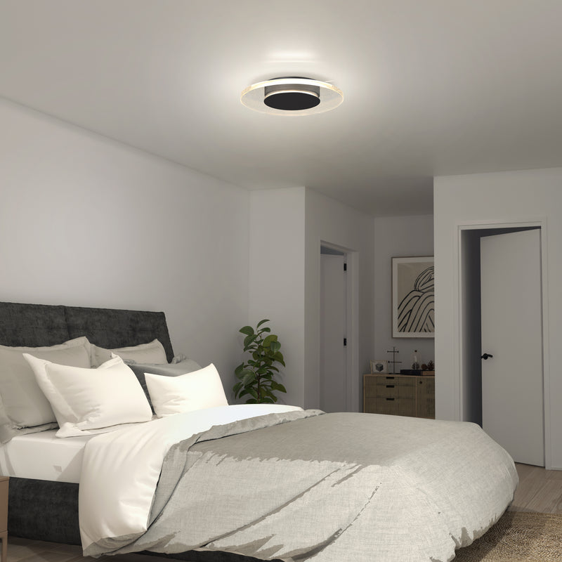 A modern bedroom features a gray upholstered bed, white and gray bedding, a small plant, a dresser with décor, and the Artika Essence Disk LED flush mount ceiling light. The walls and doors are painted white.