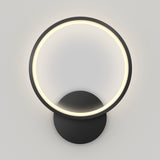 A modern wall lamp with a circular LED light ring mounted on a round black base, glowing softly against a plain light-colored wall.