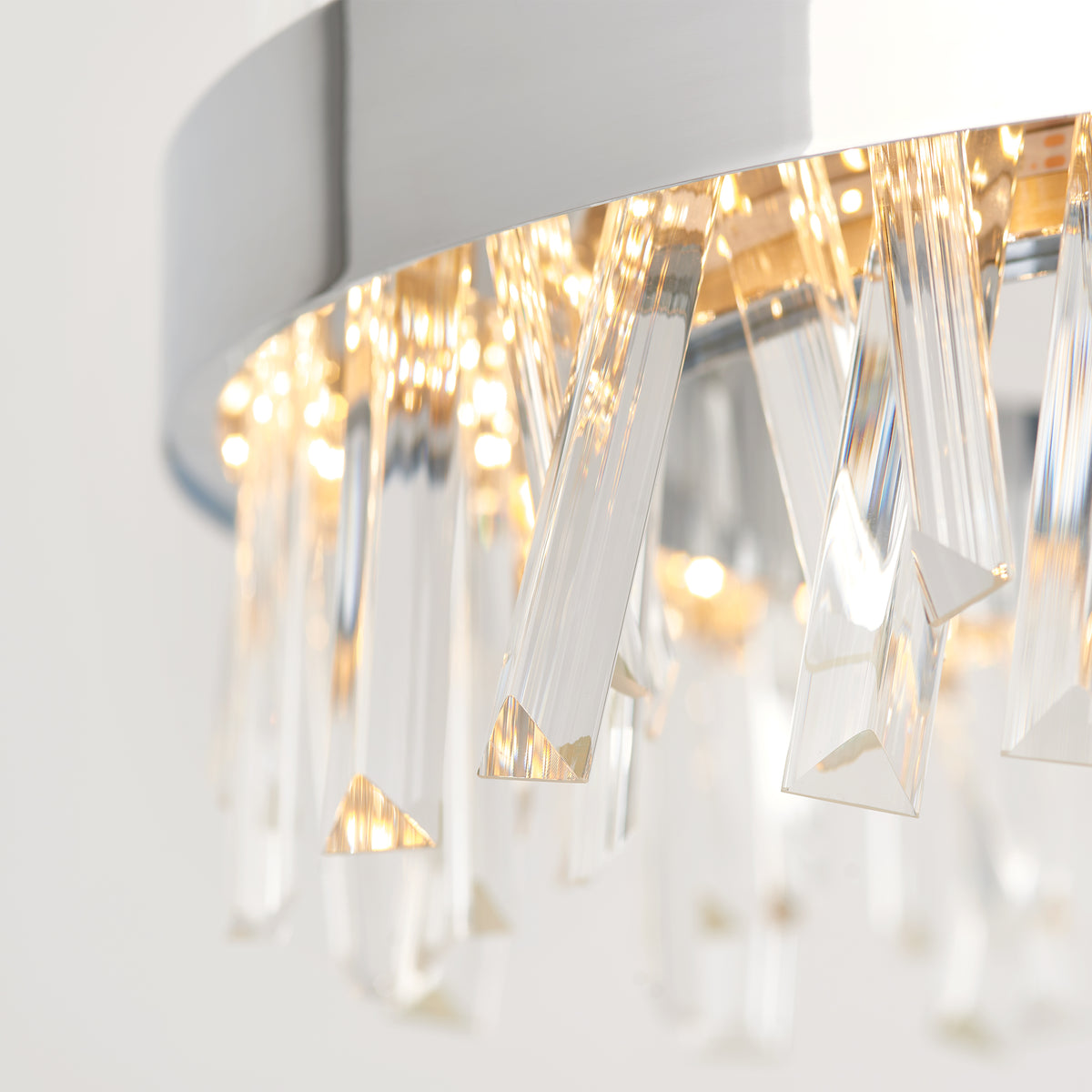 Close-up of a modern chandelier featuring elongated, clear crystal prisms hanging from a circular metal frame, with warm light reflecting through the crystals.