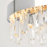 Close-up of a modern chandelier featuring elongated, clear crystal prisms hanging from a circular metal frame, with warm light reflecting through the crystals.