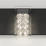 A modern wall light fixture with a clear, geometric glass cover and bright LED bulbs, mounted on a sleek, dark rectangular base against a white wall.