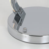 Close-up of a shiny, chrome lamp base with a small round button and the brand name artika engraved on the side. The surface reflects light and surrounding objects.