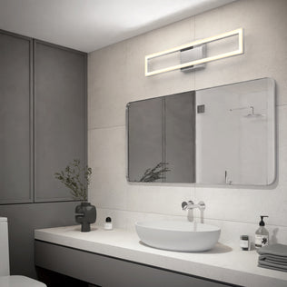 A modern bathroom with grey walls, a large rectangular mirror, an oval sink on a white countertop, a minimalist black vase with greenery, and the Artika Dover modern LED bathroom vanity light 5 CCT mounted above the mirror.