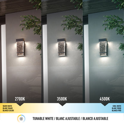 Three Artika Skyler indoor-outdoor LED wall lights mounted on a gray exterior wall display warm white (2700K), neutral white (3500K), and cool white (4500K) color temperatures, with branches and leaves visible in the foreground.