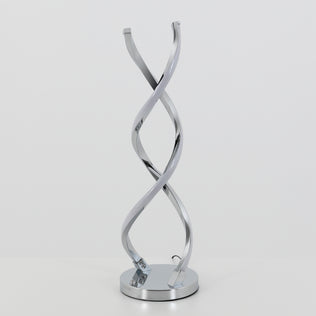The Artika Swirl LED table lamp features two intertwined, curved chrome light strips on a round base, shown against a plain white background.