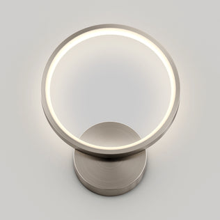 The Artika Solis modern LED indoor-outdoor wall light 5 CCT features a sleek ring design and metallic base, perfect for accent lighting in contemporary spaces, shown against a plain light gray background.