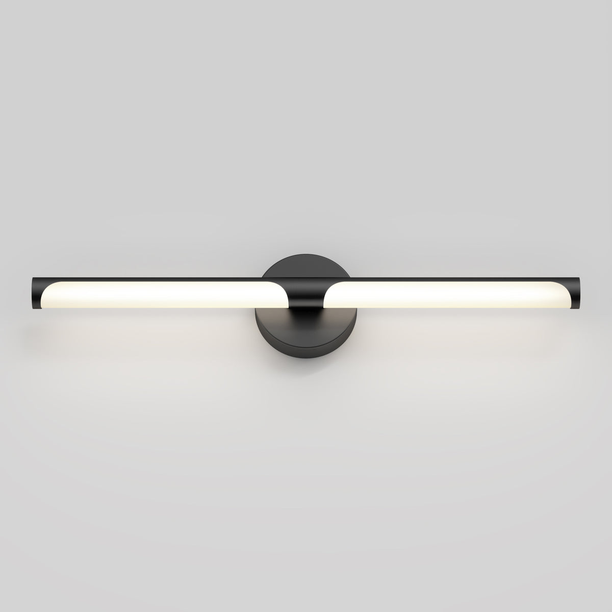 A modern, horizontal wall-mounted LED light fixture with a black circular base and sleek, tubular design, emitting soft, even white light against a plain gray background.