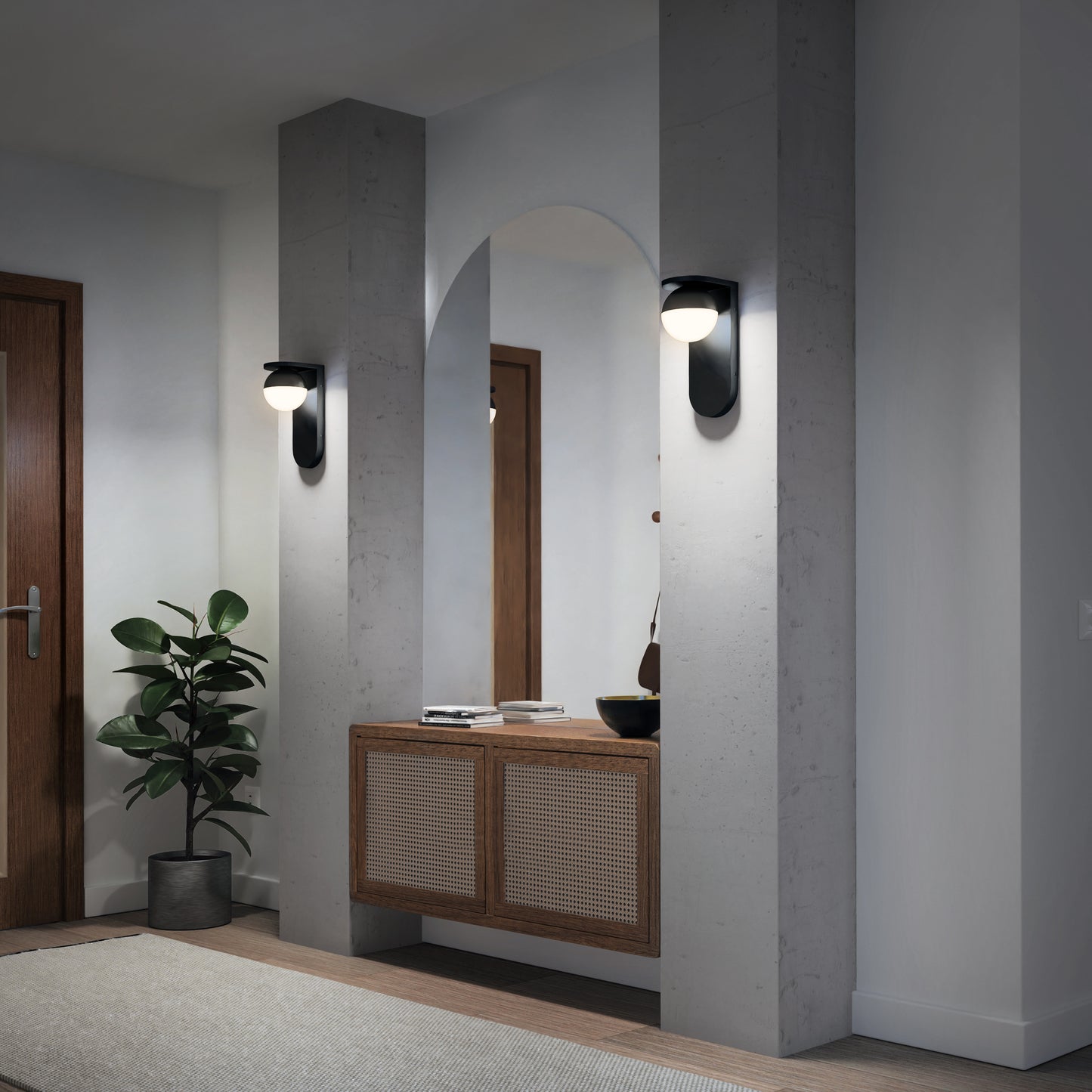 A modern hallway features two Artika Bloom indoor-outdoor LED wall lights flanking a large arched mirror above a rattan sideboard, with a potted plant on the left and a closed wooden door in the background.