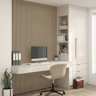A modern home office with an Artika Sonolok sound-absorbing wall panel kit, wall-mounted desk, computer, beige chair, open shelves with books and decor, drawers, a suitcase on the floor, and a potted plant beside the desk.