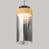 A modern pendant light with a cylindrical clear glass shade, a wooden accent near the top, and a black metal fixture, hanging against a plain gray background.