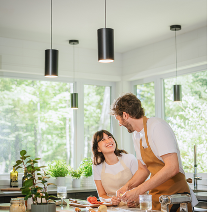 Two people cook beneath an Artika Alton mini LED pendant in a bright, modern kitchen with big windows, both smiling in aprons.