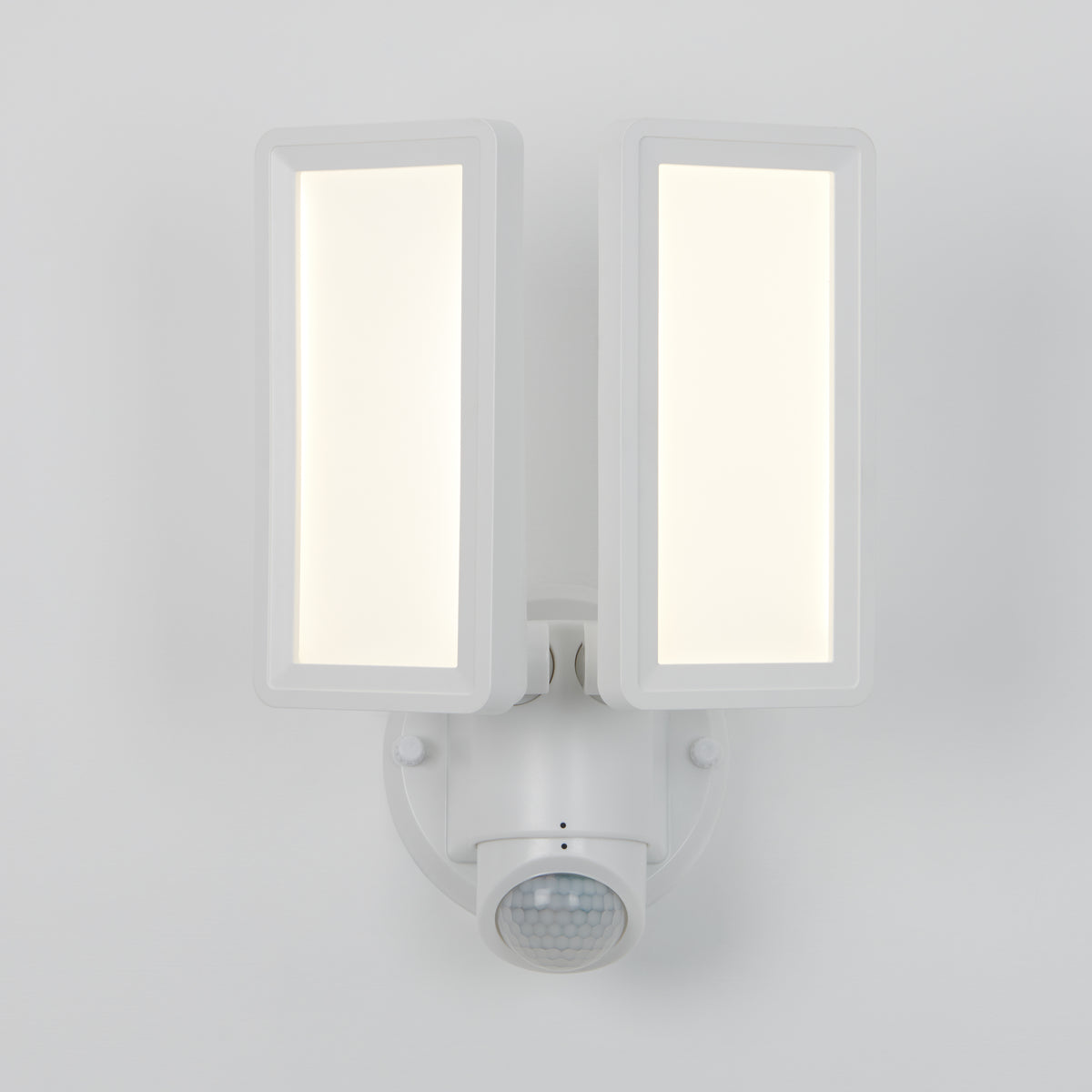 A modern white outdoor security light with two rectangular LED panels and a round motion sensor mounted on a white wall.