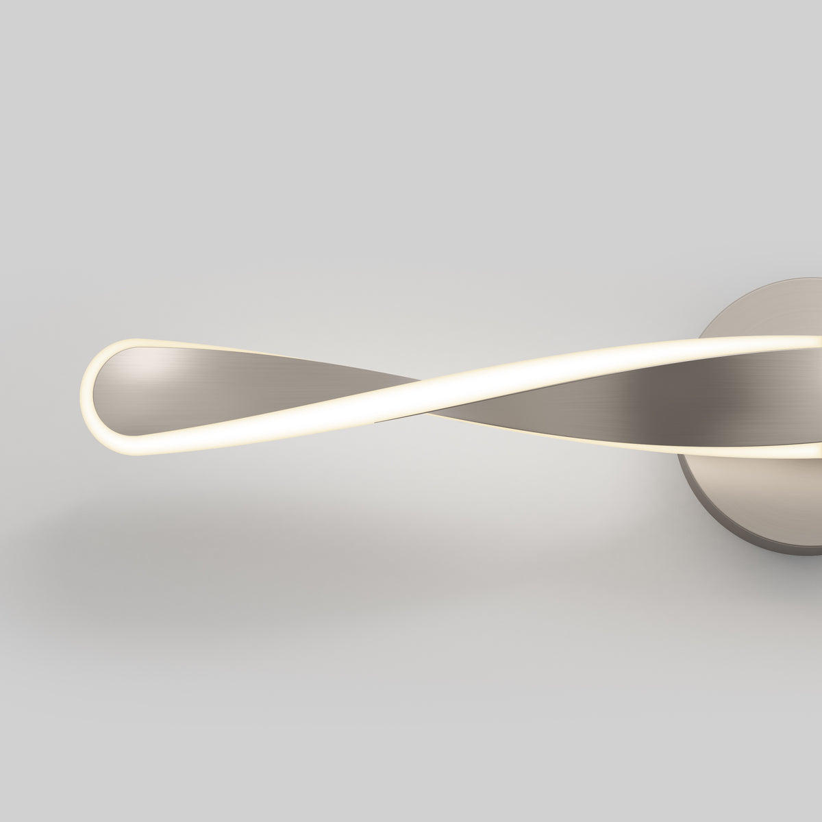 A modern ceiling light fixture with a metallic finish and an infinity loop design, emitting a soft white glow, set against a plain gray background.