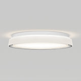 A modern, round, white ceiling light fixture emits a soft, even glow against a plain light gray background.