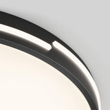 Close-up of a modern circular ceiling light with a dark frame, featuring a small gap in the frame where the light shines through, against a plain light grey background.