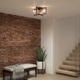 A modern interior with a brick accent wall, a bench with a gray blanket, a potted snake plant, wooden stairs with glass railing, and a black metal ceiling light fixture.