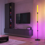 A modern living room with a wall-mounted TV, floating storage unit, shelves displaying action figures, a colorful vertical LED floor lamp, and a geometric rug on wooden floor.