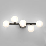 A modern wall sconce with five round frosted glass globes arranged asymmetrically on a black metal fixture, mounted on a light gray wall.